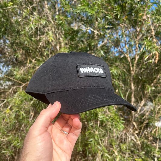Black cap with a logo held in front of green foliage, whacko